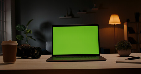 Chroma key green screen template - a laptop computer on a desk in cozy living room at night. Computer set for distance learning and remote work, technology concept 