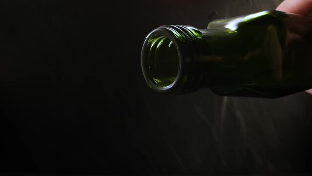 Olive oil pours from a green bottle in slow motion against a dark background