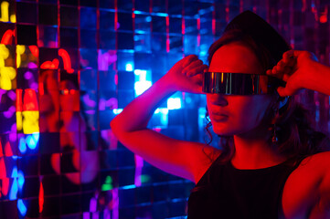 Close-up portrait of a caucasian woman in sunglasses in neon light against a mirror wall. 
