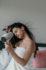 Obraz premium Shot of a young woman drying her hair in the bedroom.
