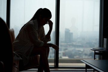 silhouette of a young woman sitting on a sofa spending time alone at home, young upset pensive...
