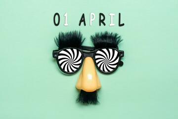 funny face - fake eyeglasses, nose and mustache, calendar date 01 April on green background Happy fools day concept 1st April party Holiday greetind card - 579926814