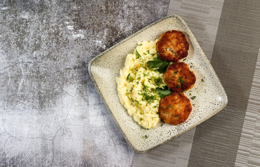 Mashed potatoes with cutlets and herbs on a square  plate on a dark background. Top view, flat lay