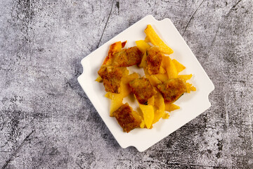 Fried fish and fried potatoes on a square  plate on a dark background. Top view, flat lay