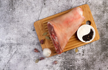 Raw pork knuckle with garlic, black pepper and bay leaves on a cutting wooden board on a dark grey background. Top view, flat lay