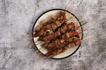 Grilled Pork Skewers on a round plate on a dark gray background. Top view, flat lay