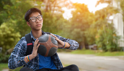 Portrait of asian male teenager in plaid shirt holding old and training basketball in hand with...