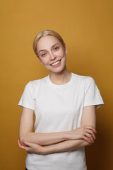 Beautiful female model in white t-shirt smiling. Friendly woman on yellow background