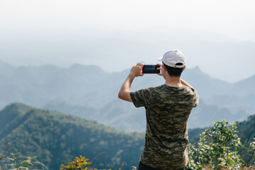 Fototapeta na wymiar Male traveler take photo top of mountain when trekking in national park of Thailand