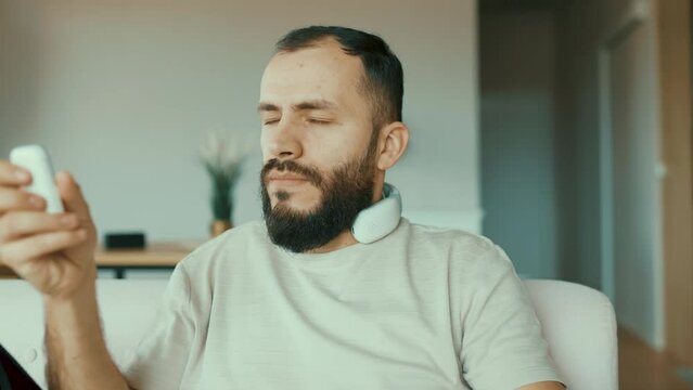 Young male wearing a device around his neck that uses vibration or other massage techniques to provide relief to sore or tense muscles in the neck and shoulders.
