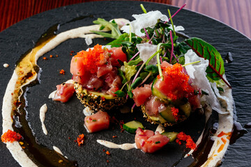 salmon tartare with sauce and herbs on a black plate