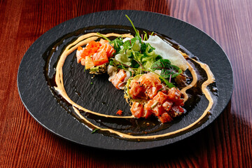 salmon tartare with sauce and herbs on a black plate