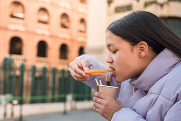 Portrait teenager eating churro at the street on Valencia city.