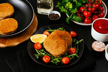 chicken cutlet on a black plate. vegetables and herbs. black bac
