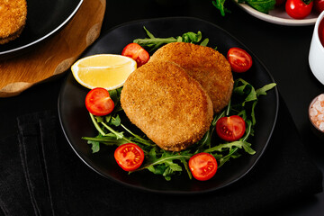 chicken cutlet on a black plate. vegetables and herbs. black bac