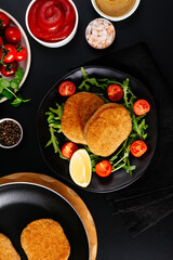 chicken cutlet on a black plate. vegetables and herbs. black bac