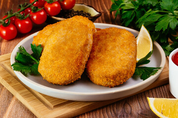 chicken cutlet on a plate. vegetables and herbs. wooden table
