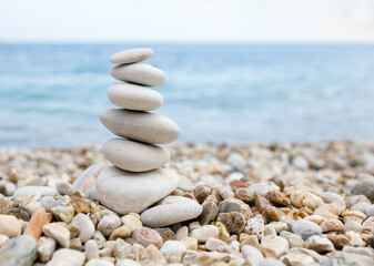 Fototapeta na wymiar A balance of pebble stones is built on a stone beach against the backdrop of the blue sea.