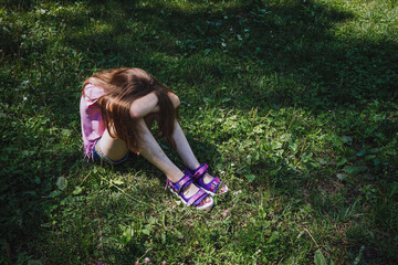 Girl girl's sitting on the grass hiding her face