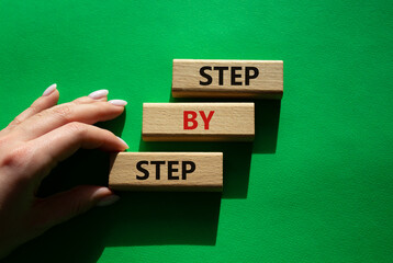 Step by step symbol. Wooden blocks with words Step by step. Beautiful green background. Businessman hand. Business concept. Copy space.