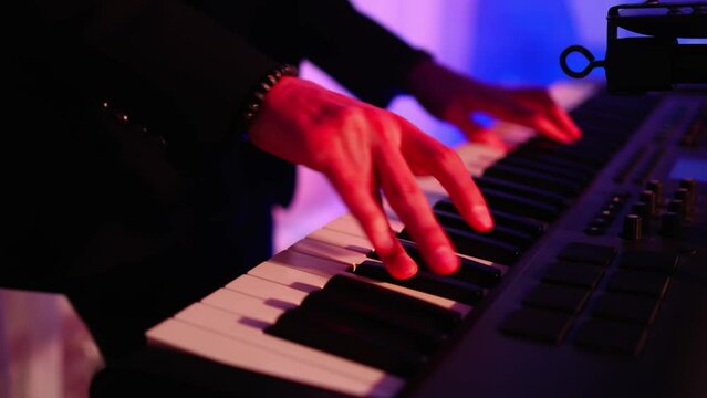 Male hands playing on synthesizer piano. Band at concert stage playing music.