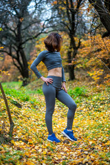 A slender woman in leggings and a crop top poses in the autumn forest.