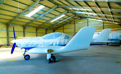 small plane with athree bladed propeller of private aviation is covered with cover in bright hangar...