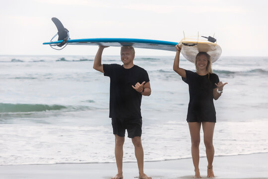 Full length portrait of smiling friends gesturing while carrying surfboards on head at beach