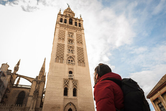 Low angle view of backpacker looking at La Giralda in Seville Cathedral against cloudy sky in city
