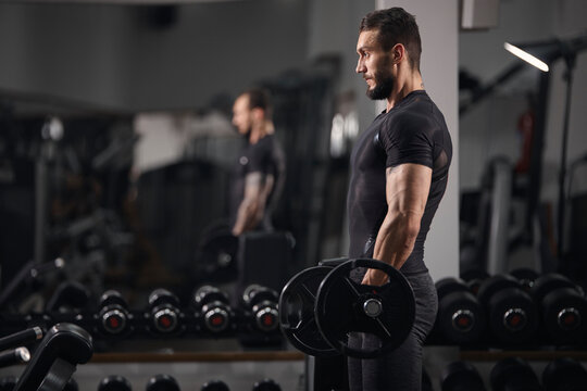 Side view of man lifting barbell while exercising at gym