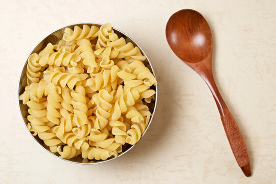 Overhead view of uncooked rotini pasta in container with wooden spoon on table