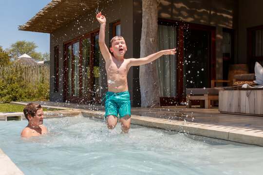 Shirtless playful boy jumping while brother swimming in plunge pool against house during summer