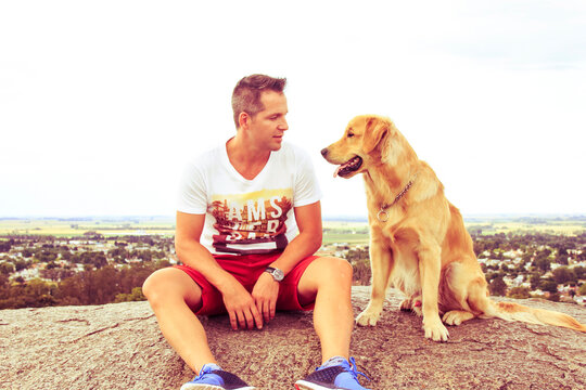 Full length of mid adult man looking at dog while sitting on rock against clear sky