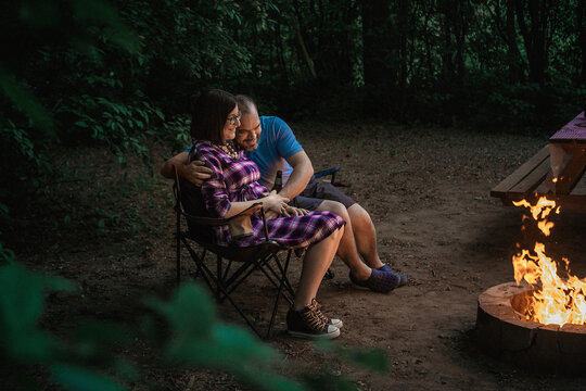 Full length of loving couple sitting on camping chairs by campfire at forest