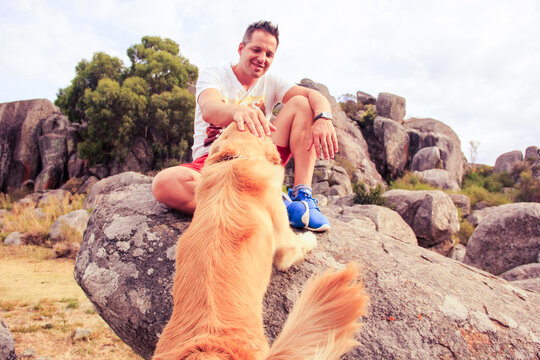 Smiling mid adult man petting dog while sitting on rock
