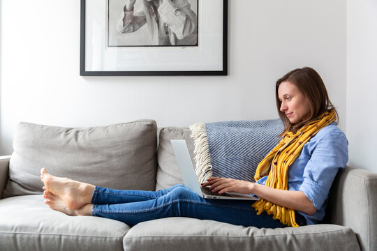 Side view of woman using laptop computer while sitting on sofa in living room