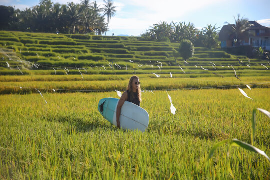 Woman with surfboard walking on grassy field against sky