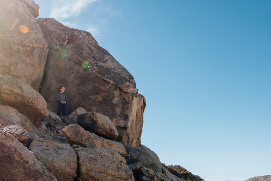 Low angle view of boy standing on rocks against sky during summer