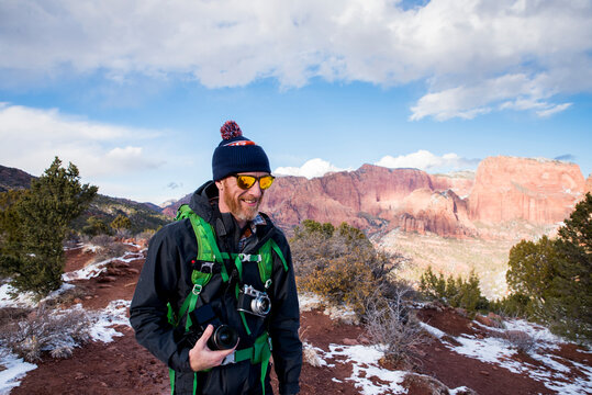 Smiling hiker with cameras standing at desert during winter