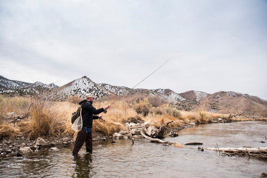 Man fishing in river against mountains and sky