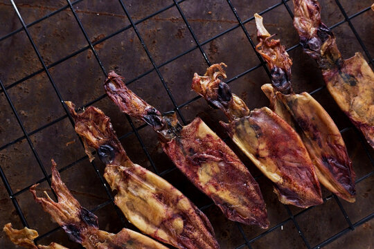 Overhead view of dried roasted squids on metal grate over table