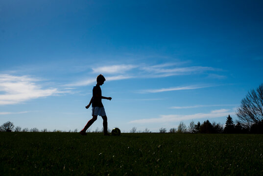 Side view of boy playing soccer on field against sky