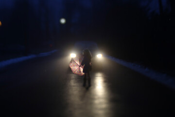 Silhouette girl with umbrella standing by car on road during winter at night