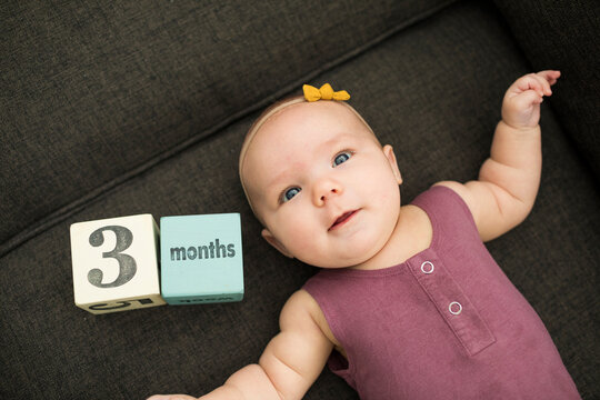 High angle view of cute baby girl lying with toy blocks on sofa at home