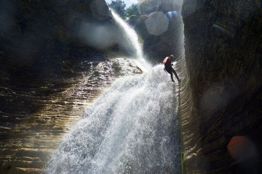 Low angle view of male hiker rappelling on canyon amidst waterfall