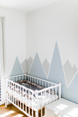 Kinderzimmer in Blautönen mit Gitterbett und Bergen an der Wand