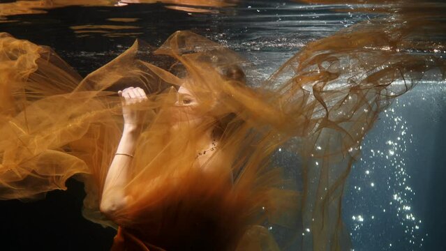 Girl underwater in the pool of a photo studio in a dress.