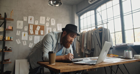 A male hipster clothing designer working in his office, redrawing his sketches to graphics tablet,...
