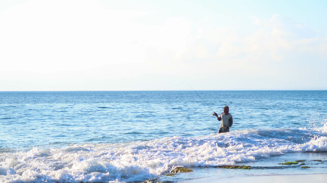 A man is fishing in the rocky sea in Bali, Indonesia. Angler fishing on a choppy beach during the day.