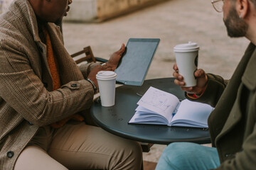 Obraz premium Close up shot of black male person working on tablet and explaining something to his white male colleague